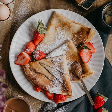 Crêpe sucrée avec fraises et garnitures sur assiette blanche au Petit Poucet